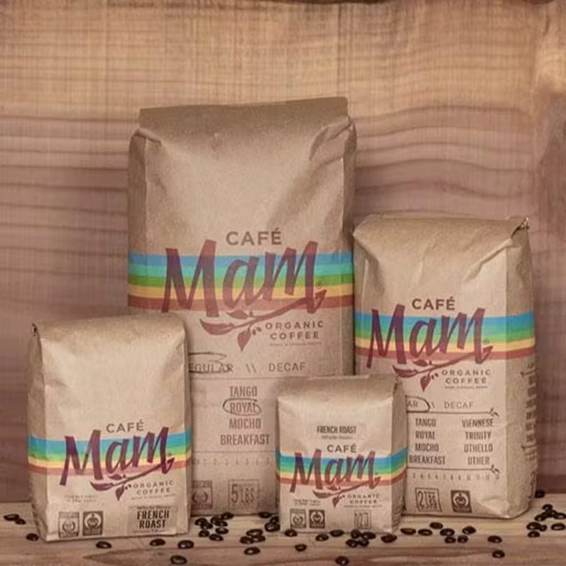 Four bags of "Café Mam Organic Coffee" in various sizes, with coffee beans scattered around.